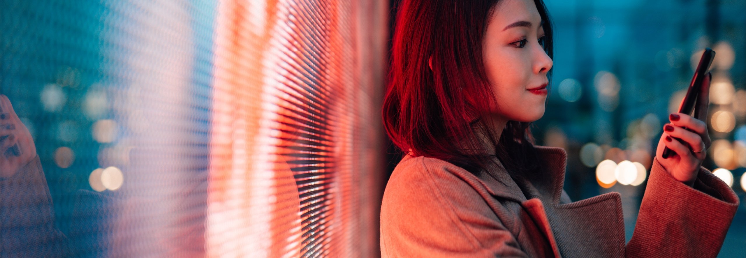 Woman leaning against digital wall at night while working on smartphone