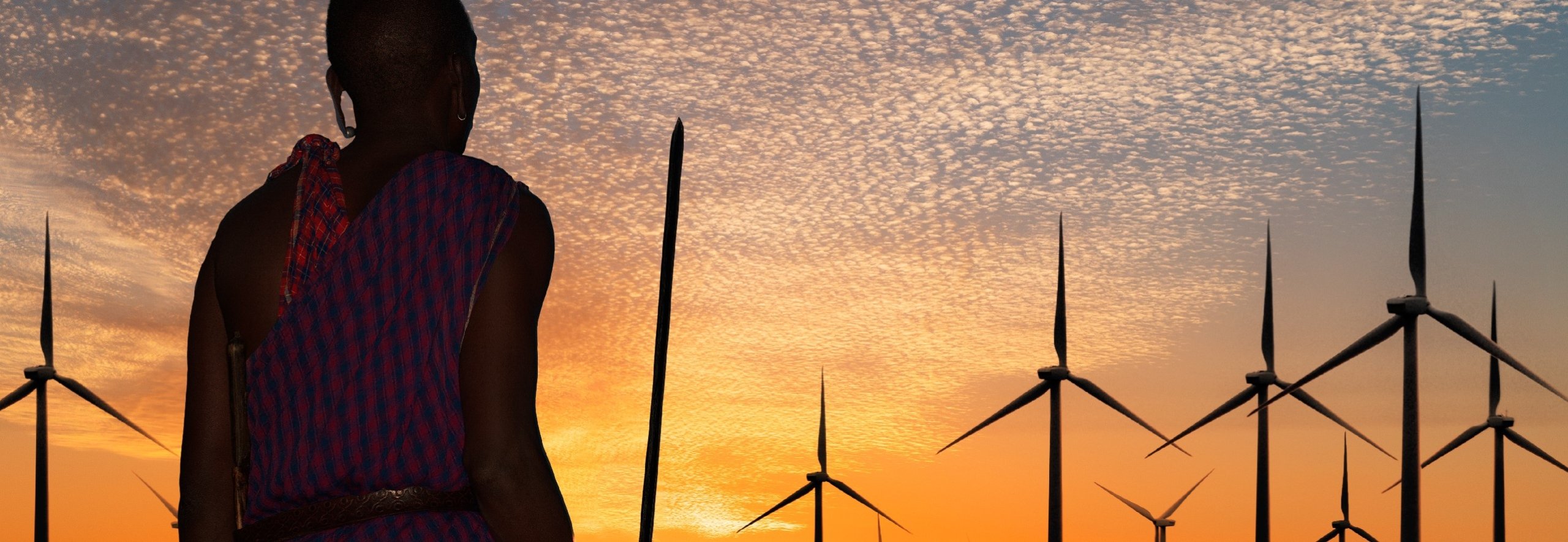 Rear view of a Masai warrior wearing traditional clothes watching wind turbines at sunset