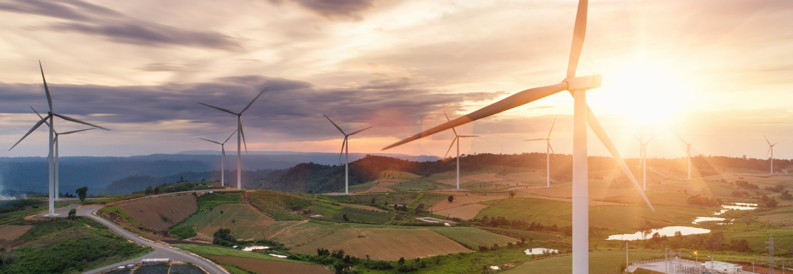 Wind turbines on top of green hills on a cloudy day with a ray of sunshine