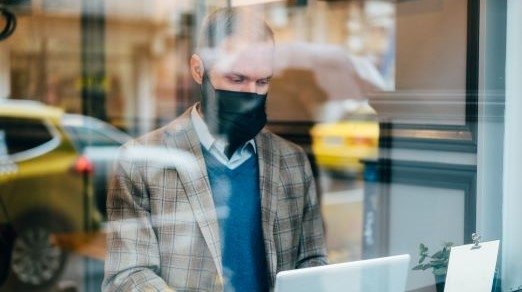 image of man with mask on working on laptop offsite