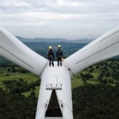 Two workers standing on top of a wind turbines